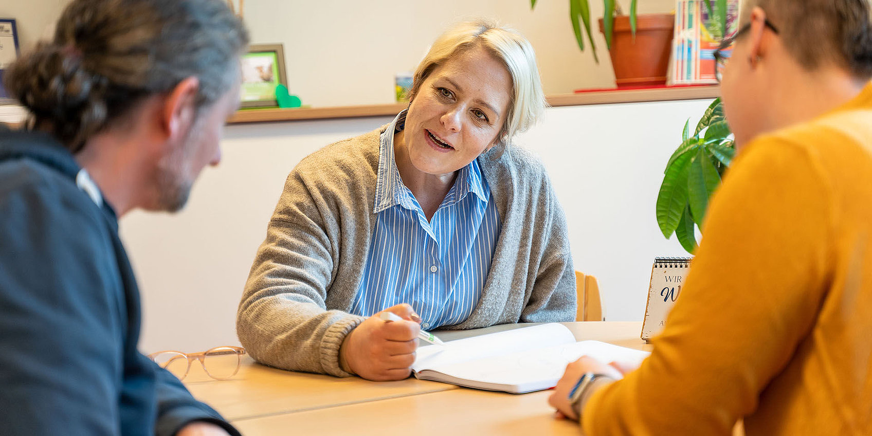 Drei Personen bei Beratungsgespräch eine Person zeigt Notizen
